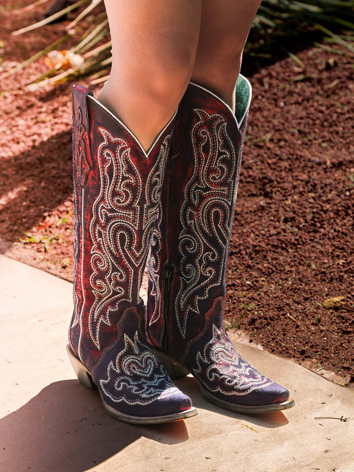 Woman wearing Corral A4772 red tall cowboy boots with blue and white chameleon embroidery and crystals, styled outdoors for bold Western fashion